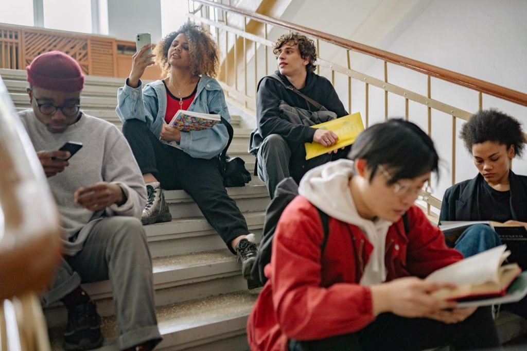 College students sitting on stairs, studying and using phones in a university setting.